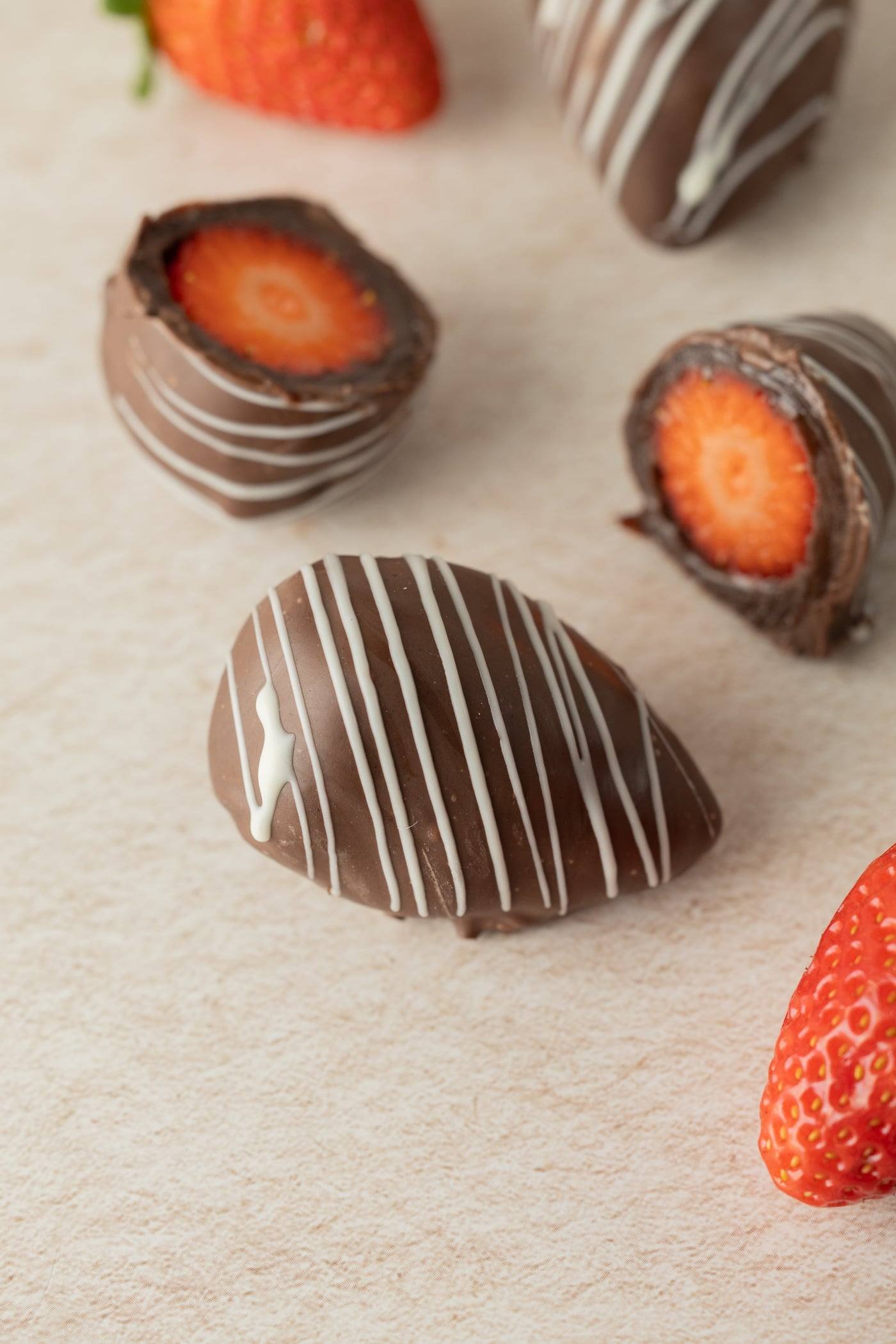 Morangos cobertos com chocolate ao leite e fios de chocolate branco; dois deles cortados ao meio mostram o morango inteiro por dentro.