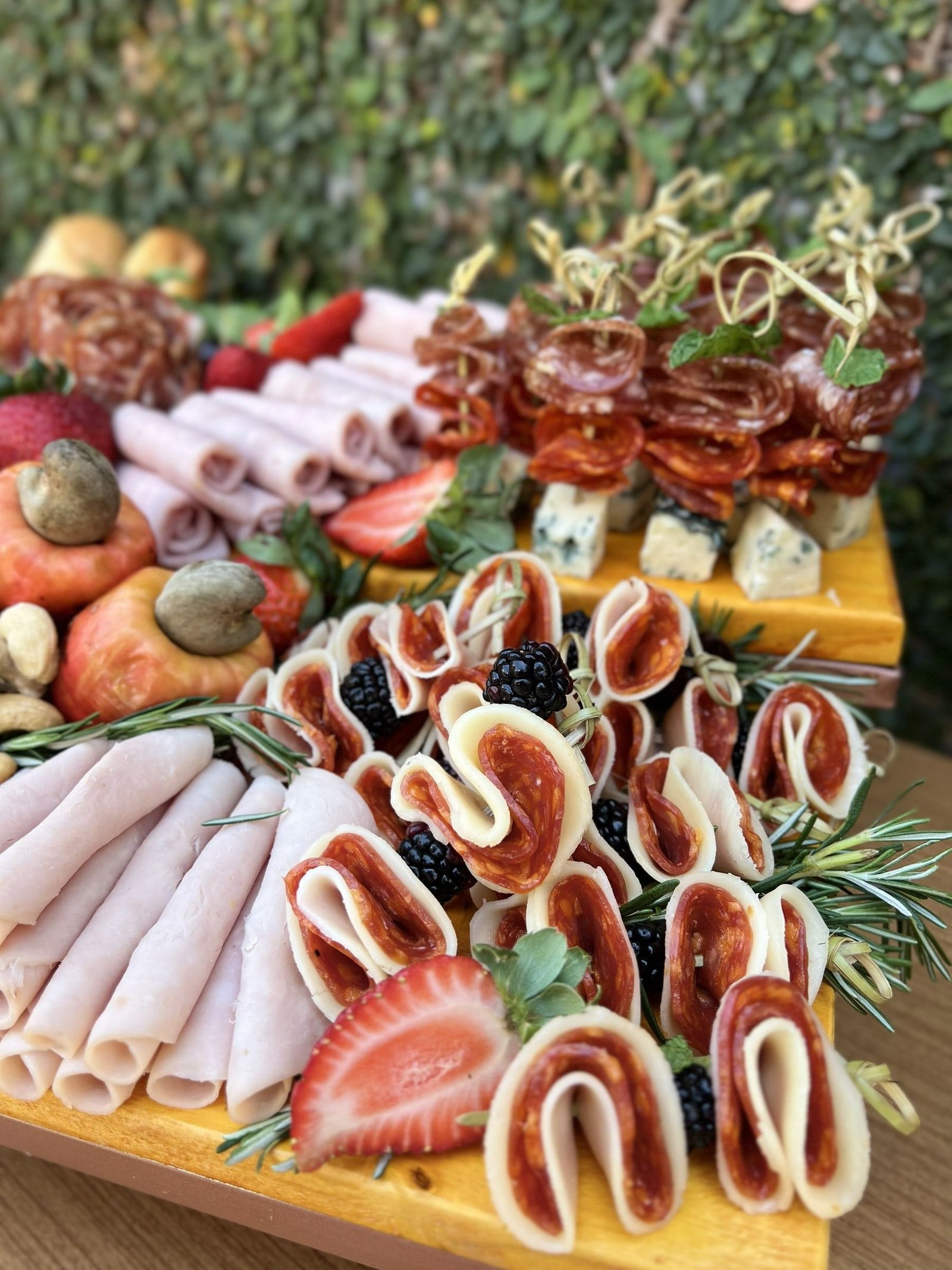 Tábua com frios enrolados, salame, morangos, amoras e queijo, com espetinhos de salame ao fundo.