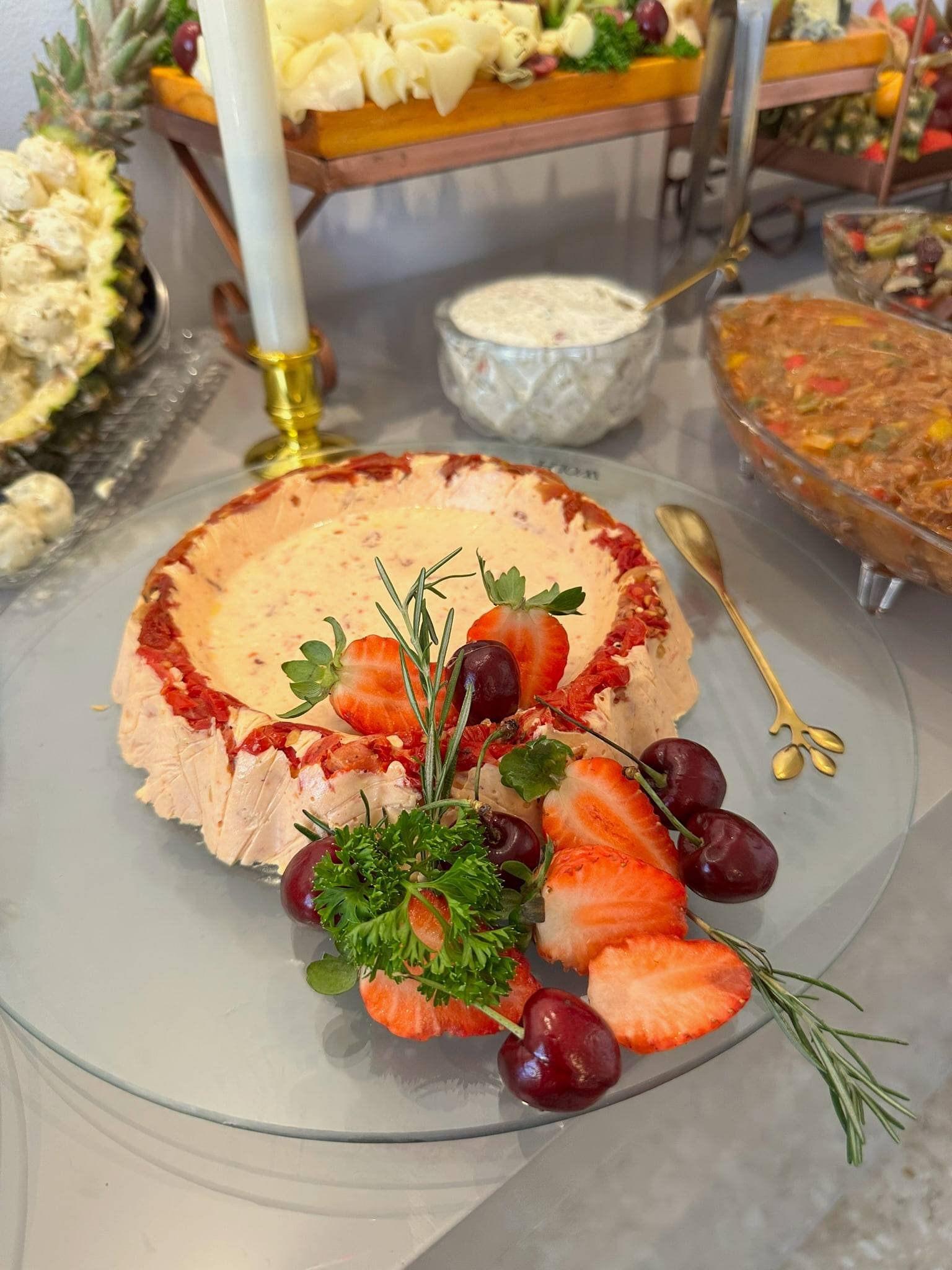 Torta cremosa em formato de coroa decorada com morangos, cerejas e ervas, em prato de vidro.